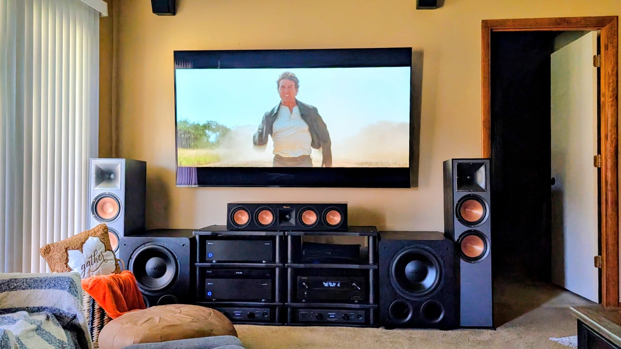 Large framed flat screen TV wall mounted above a two bay audio component rack, with Klipsch towers either side and a center channel speaker